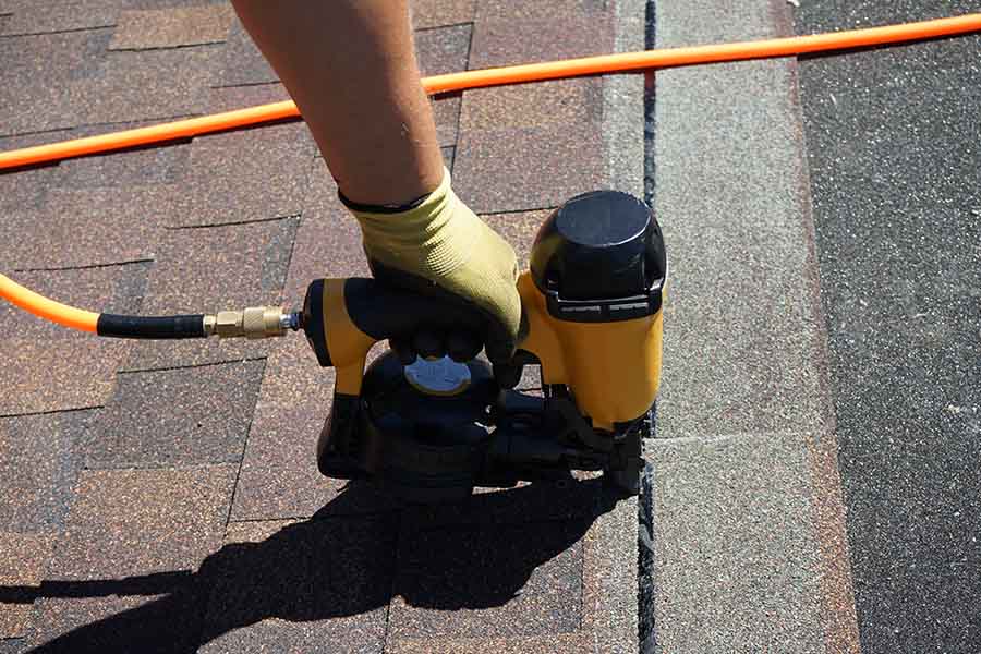 Roofer installing shingles with nail gun